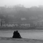 Silhouette of person sitting on rock near body of water