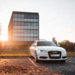 White Audi sedan parked on concrete parking area surrounded by dried leaves